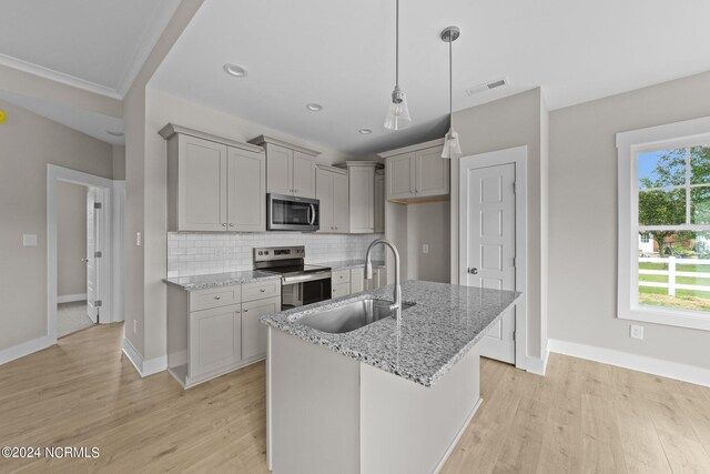 kitchen with light stone counters, sink, hanging light fixtures, light hardwood / wood-style flooring, and appliances with stainless steel finishes