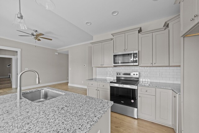 kitchen with light hardwood / wood-style floors, sink, decorative backsplash, stainless steel appliances, and ceiling fan