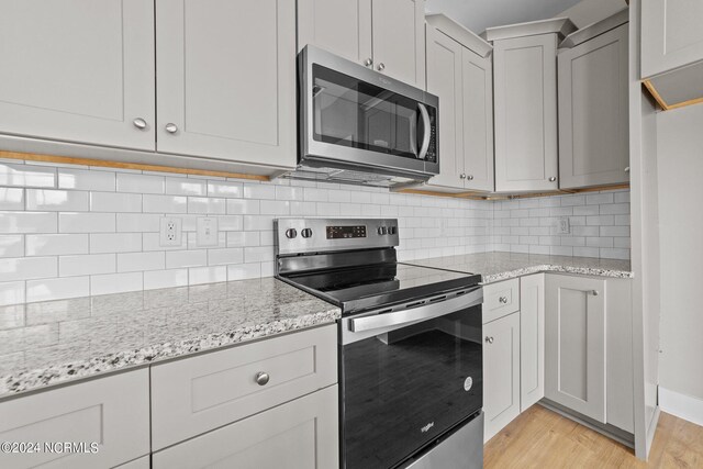 kitchen with appliances with stainless steel finishes, decorative backsplash, light wood-type flooring, and light stone countertops