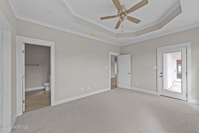 unfurnished bedroom featuring a raised ceiling, connected bathroom, crown molding, ceiling fan, and light carpet