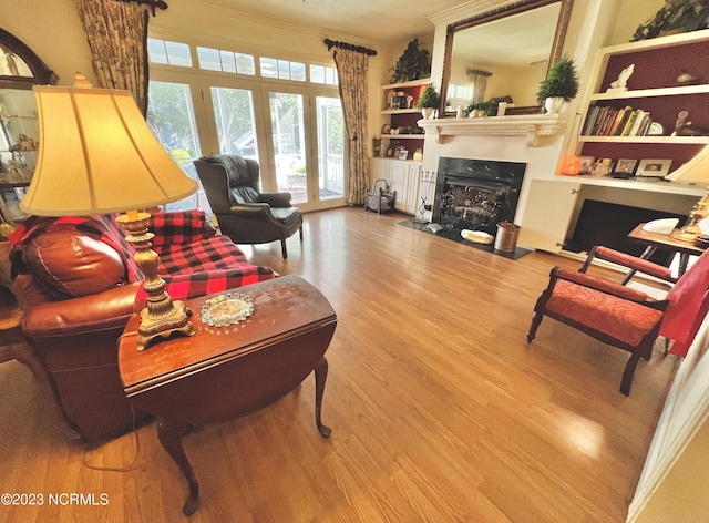 living room featuring built in shelves, ornamental molding, light hardwood / wood-style floors, and french doors