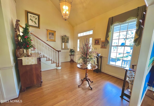 foyer entrance with light hardwood / wood-style flooring, high vaulted ceiling, and an inviting chandelier