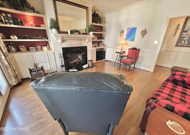 living room featuring built in shelves, light hardwood / wood-style floors, and crown molding