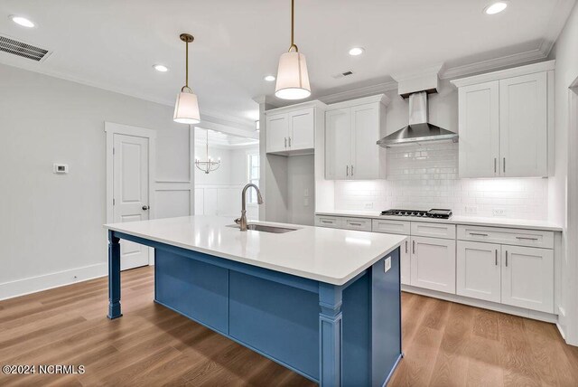 kitchen with hanging light fixtures, light hardwood / wood-style flooring, sink, and wall chimney range hood