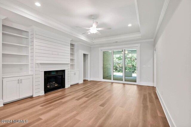 unfurnished living room with light wood-type flooring, built in shelves, a raised ceiling, ceiling fan, and ornamental molding