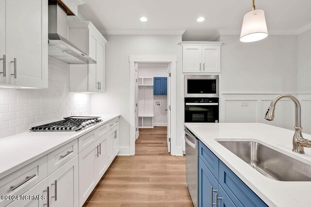 kitchen featuring crown molding, hanging light fixtures, sink, white cabinetry, and wall chimney range hood