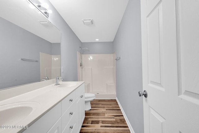 bathroom with a shower, dual bowl vanity, toilet, and wood-type flooring