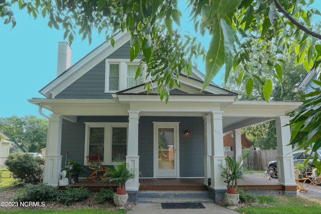 view of front facade featuring covered porch, a chimney, and fence