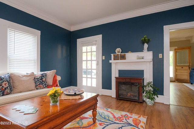 living area with baseboards, a glass covered fireplace, crown molding, and wood finished floors