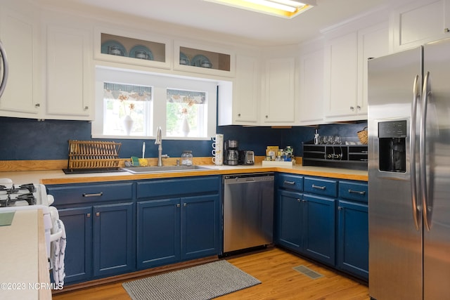 kitchen with appliances with stainless steel finishes, blue cabinets, light countertops, white cabinetry, and a sink