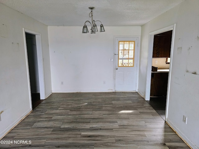 unfurnished dining area featuring dark hardwood / wood-style flooring, a chandelier, and a textured ceiling