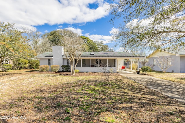 view of front of property featuring concrete driveway, a sunroom, a chimney, an attached carport, and a front lawn