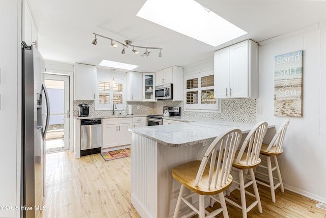 404 Mercer St, Oak Island, NC 28465 - kitchen featuring stainless steel appliances, a skylight, a peninsula, light wood-style floors, and plenty of natural light
