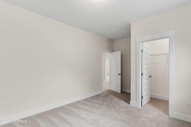 unfurnished bedroom with a walk in closet, a closet, and light carpet