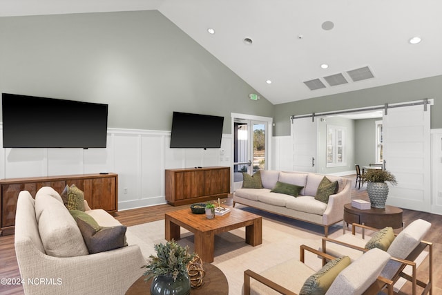 living room with light hardwood / wood-style flooring, high vaulted ceiling, and a barn door