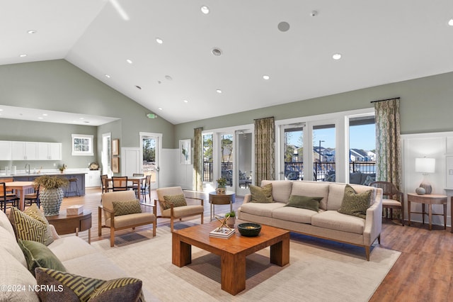 living room with high vaulted ceiling, sink, and light hardwood / wood-style floors