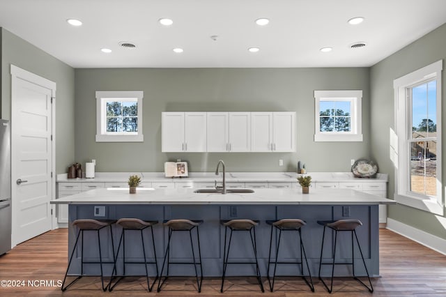 kitchen featuring a kitchen island with sink, sink, white cabinetry, and a breakfast bar