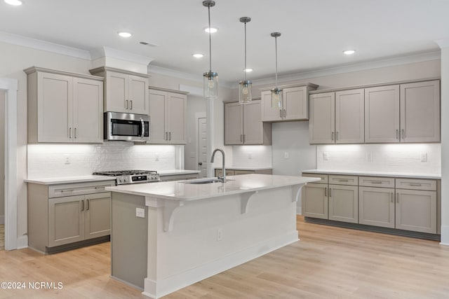 kitchen featuring decorative light fixtures, an island with sink, sink, stove, and light wood-type flooring