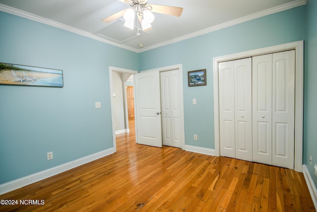 unfurnished bedroom featuring ceiling fan, light hardwood / wood-style floors, crown molding, and multiple closets