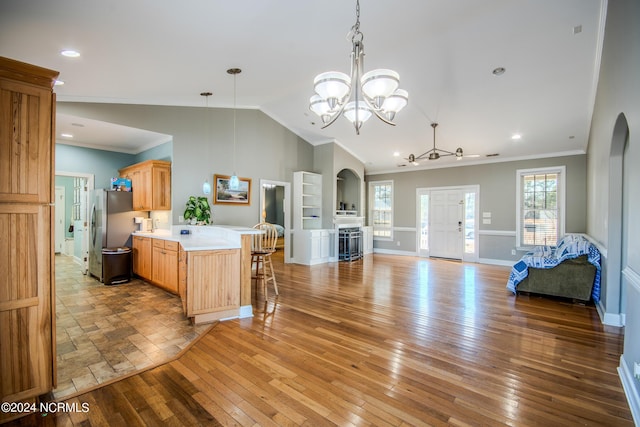 kitchen with pendant lighting, crown molding, light wood-type flooring, kitchen peninsula, and stainless steel refrigerator