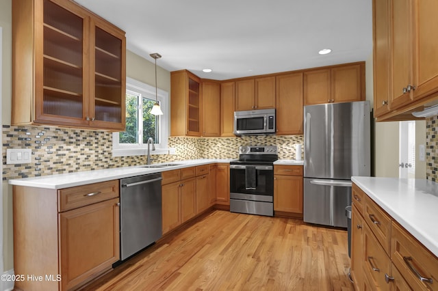 kitchen with appliances with stainless steel finishes, light wood-type flooring, a sink, decorative backsplash, and hanging light fixtures