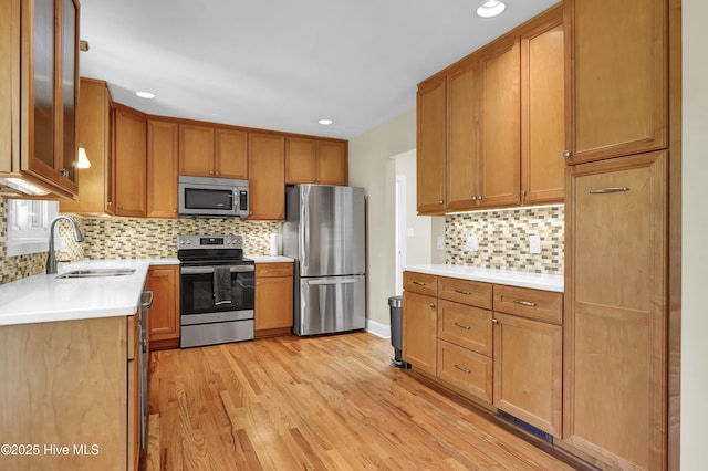 kitchen featuring stainless steel appliances, a sink, backsplash, light wood-style flooring, and light countertops