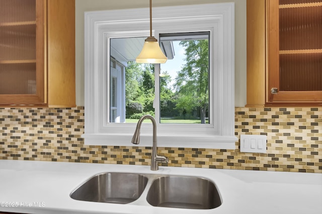 kitchen view of a sink, light countertops, backsplash, and brown cabinetry