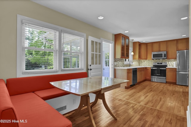 kitchen with stainless steel appliances, light wood-type flooring, light countertops, decorative backsplash, and brown cabinets