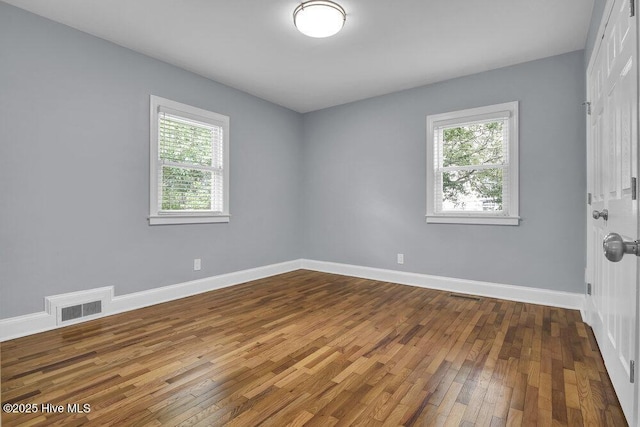 empty room featuring healthy amount of natural light, wood-type flooring, and baseboards