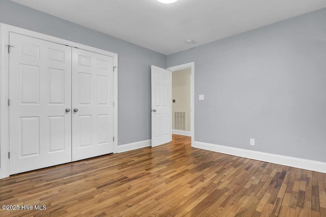 unfurnished bedroom with wood finished floors, baseboards, and a closet