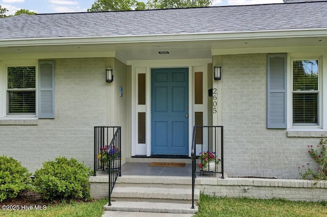 view of exterior entry with brick siding and a shingled roof