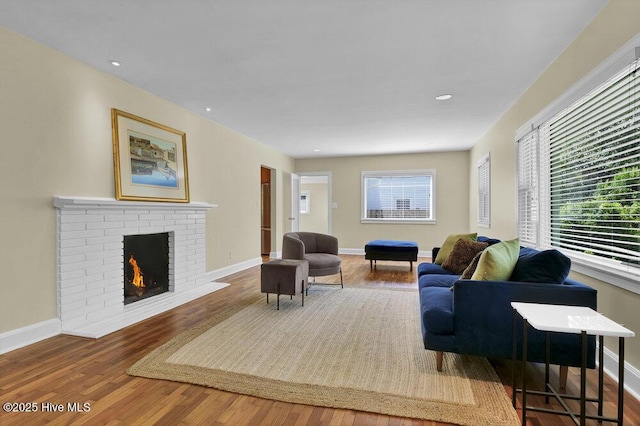 living room with healthy amount of natural light, wood finished floors, a brick fireplace, baseboards, and recessed lighting