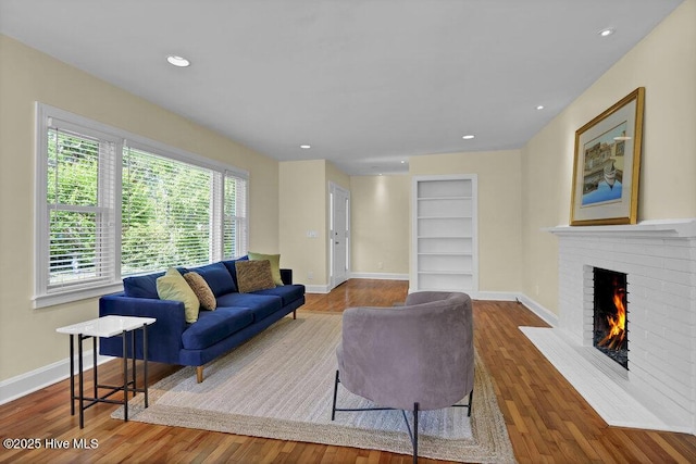 living area featuring built in features, a brick fireplace, wood finished floors, baseboards, and recessed lighting
