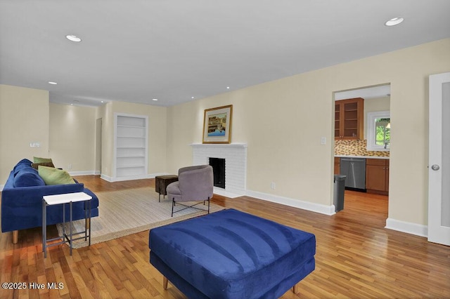 living area with light wood-style flooring, built in shelves, a fireplace, baseboards, and recessed lighting
