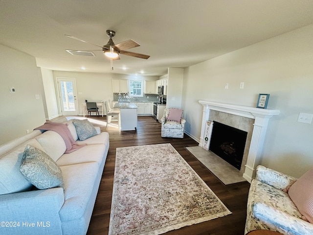 living room featuring a tile fireplace, ceiling fan, and dark wood-type flooring