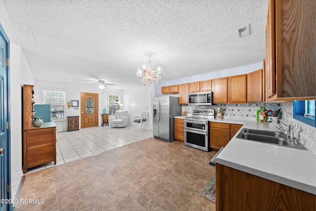 kitchen with appliances with stainless steel finishes, tasteful backsplash, light tile floors, ceiling fan with notable chandelier, and sink