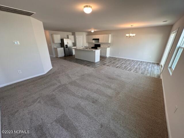 unfurnished living room featuring dark colored carpet and a chandelier