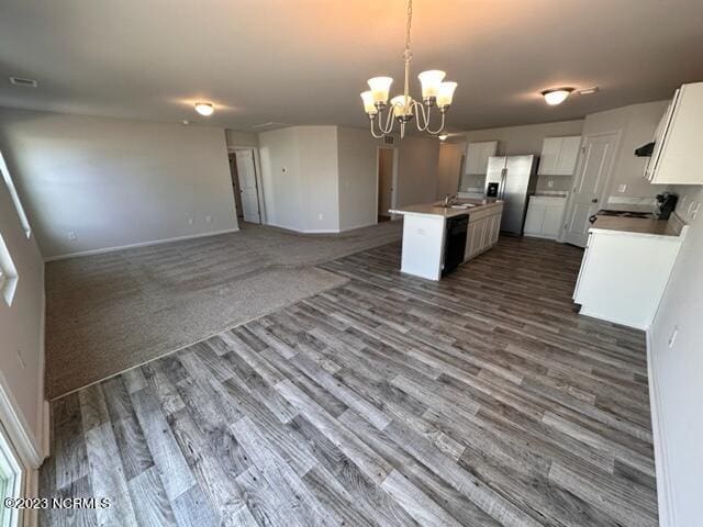 kitchen featuring hanging light fixtures, dark carpet, an island with sink, a notable chandelier, and stove