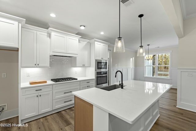 kitchen featuring visible vents, a wainscoted wall, appliances with stainless steel finishes, ornamental molding, and a sink