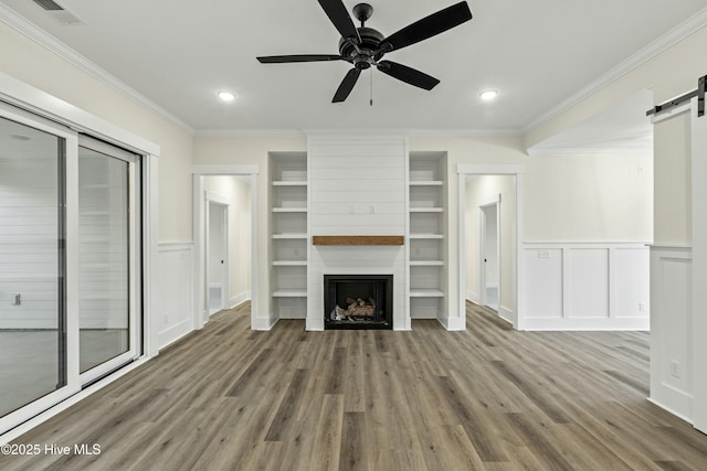 unfurnished living room featuring a barn door, a decorative wall, a large fireplace, wood finished floors, and crown molding