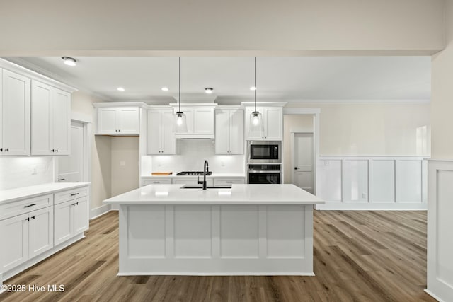 kitchen with ornamental molding, appliances with stainless steel finishes, an island with sink, and white cabinets