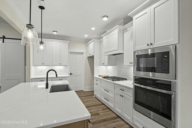 kitchen with a barn door, a sink, light countertops, ornamental molding, and appliances with stainless steel finishes