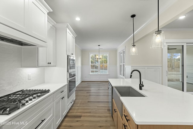 kitchen featuring a wainscoted wall, ornamental molding, dark wood-type flooring, stainless steel appliances, and light countertops