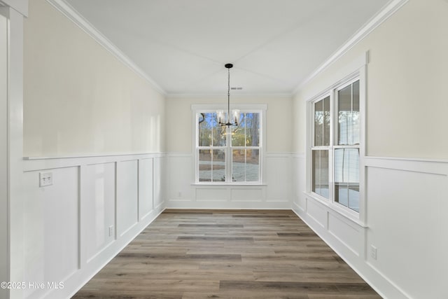 unfurnished dining area featuring a notable chandelier, visible vents, ornamental molding, wainscoting, and wood finished floors