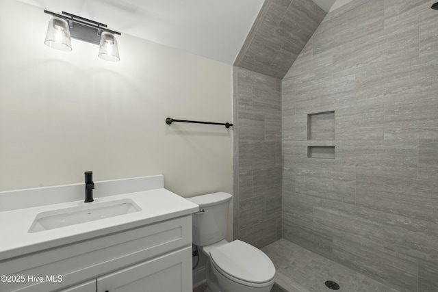 bathroom with toilet, lofted ceiling, tiled shower, and vanity