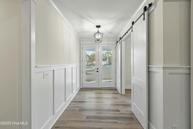 doorway to outside with ornamental molding, a barn door, wood finished floors, and a decorative wall