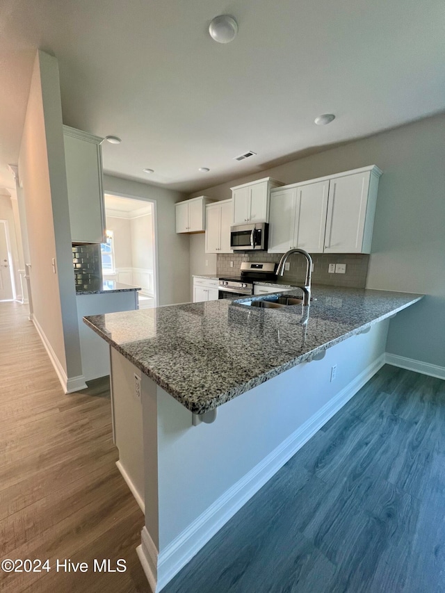 kitchen featuring hardwood / wood-style floors, kitchen peninsula, tasteful backsplash, white cabinetry, and stainless steel appliances