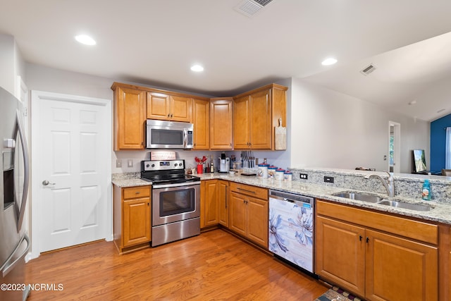 kitchen with light hardwood / wood-style flooring, stainless steel appliances, sink, kitchen peninsula, and light stone countertops