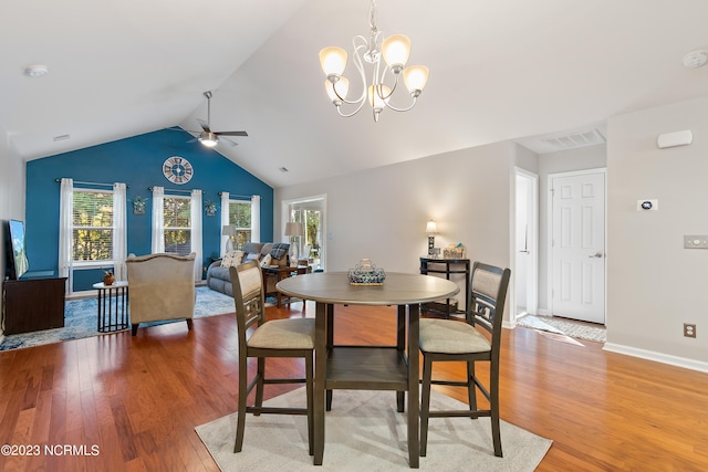 dining room with ceiling fan with notable chandelier, wood-type flooring, and vaulted ceiling