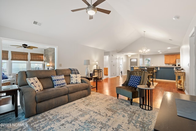 living room featuring light hardwood / wood-style flooring, ceiling fan with notable chandelier, and high vaulted ceiling